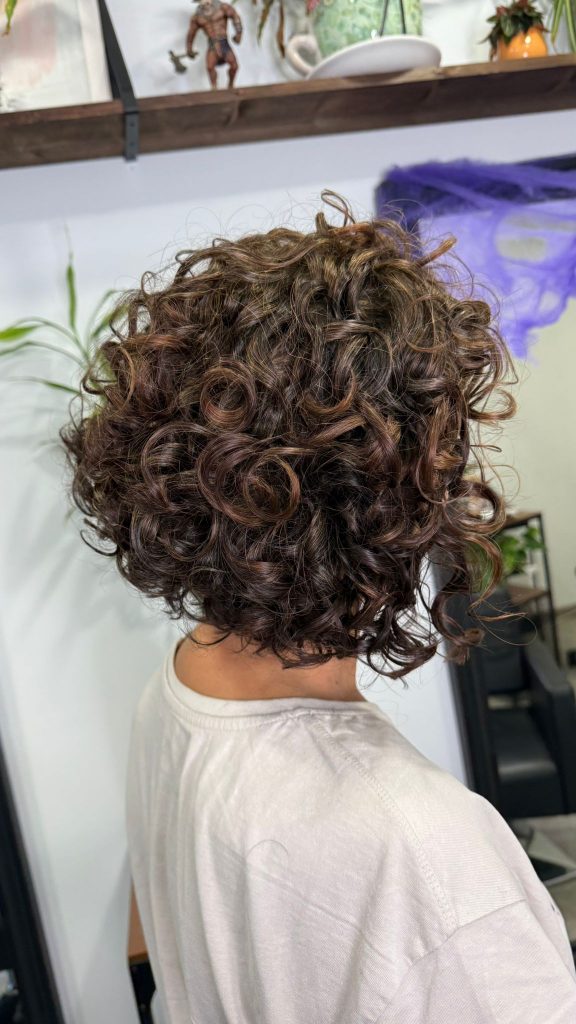 Cabello con coloración vegetal vista lateral, tonos castaños profundos con definición de rizos y brillo natural