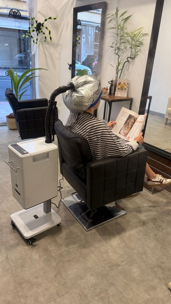 Persona disfrutando de un tratamiento capilar Bloom! + Spa Mist en Iconixs Peluquería, relajada bajo la bruma hidratante mientras lee una revista