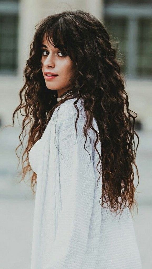 Camila Cabello con corte shaggy rizado y flequillo largo desenfadado, cabello castaño oscuro con movimiento natural inspirado en los setenta

